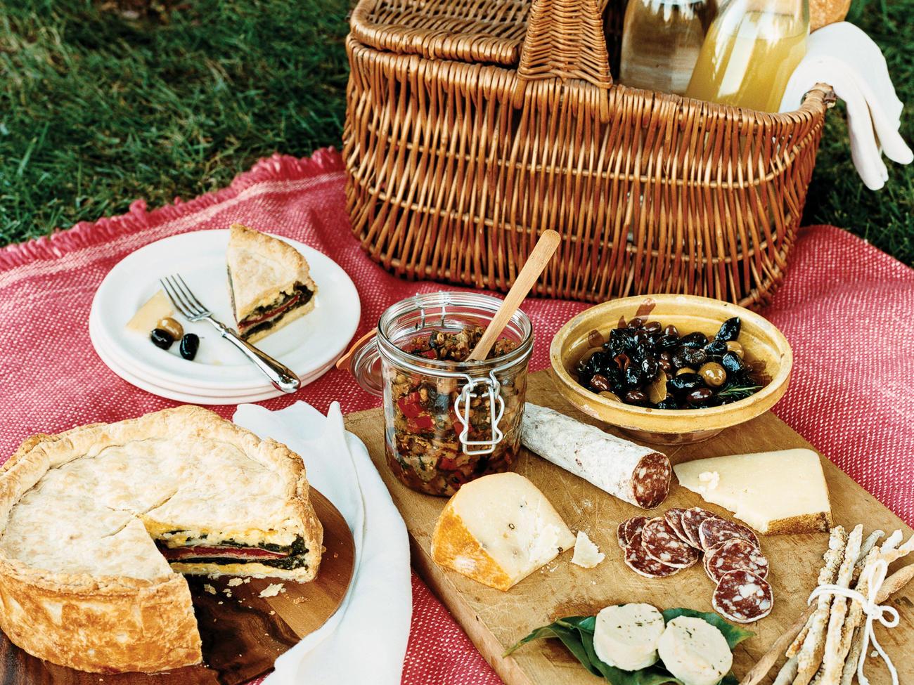 est picnic spots in the Cape Winelands featuring a gourmet spread of artisan cheeses, cured meats, fresh bread, olives and savoury tarts on a picnic blanket.